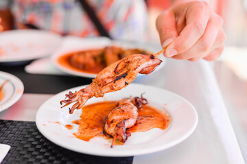 Grilled Squids on wooden sticks on white plate in spicy sause. A dish of Chinese cuisine.