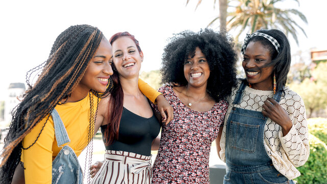 Friendly multiracial group of female friends cuddling on street while spending weekend in summer together