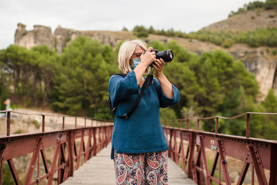 Travelling female photographer with professional photo camera standing on old bridge and taking pictures while exploring views of Cuenca town in Spain