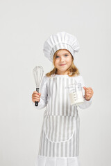 Naklejka premium little girl in chef hat and apron with flour in measuring cup and whisk. child dreams of becoming a chef.