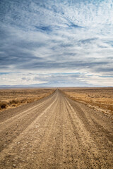 empty dirt road in the desert leading to mountains with blue sky and clouds