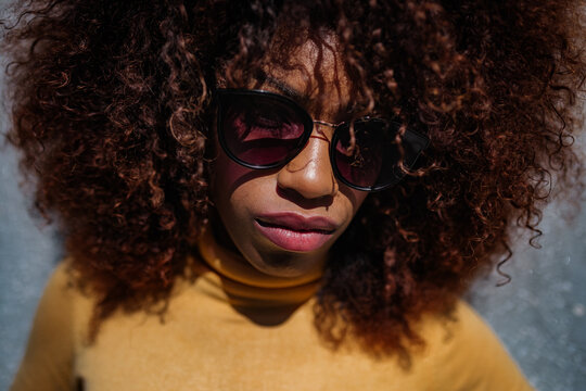Black woman with afro hair posing in front of a gray wall looking at camera