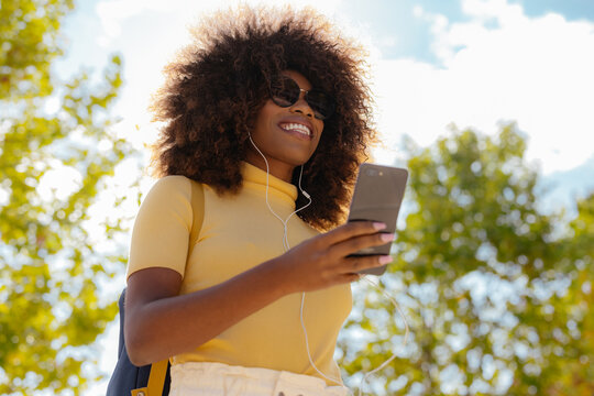 Black woman with afro hair listening to music on mobile with a backpack on her back