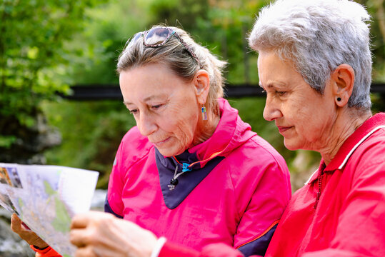 Senior female hikers watching paper map on mountain behind Casano river in Spain