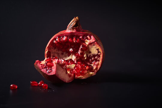 Fresh ripe halved pomegranate and seeds on black background