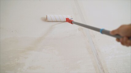 Worker priming with a paint roller. Primer worker with paint roller. white primer painting with roller brush on the repair cement wall construction background