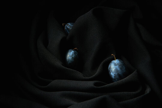 Some grapes on thin stems placed on dark black wrinkled cloth in studio