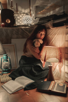 Young charming female embracing bouquet of blossoming delicate flowers looking at camera on cozy room with dim orange light
