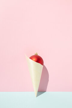 Top view of red shiny Christmas ball in paper cone in shape of ice cream placed on pink background