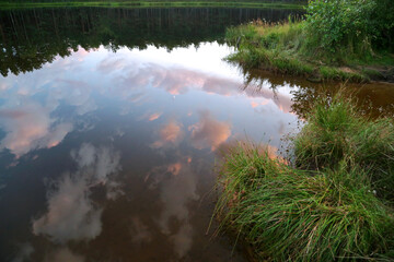 Summer ride with a forest lake in which clouds are reflected during sunset