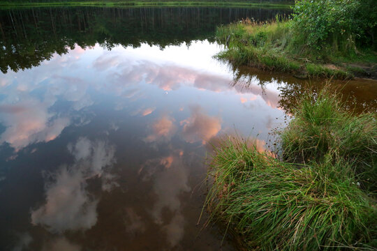 Summer ride with a forest lake in which clouds are reflected during sunset