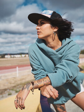 Determined tattooed female in clothes in street style standing in city on sunny day and looking away