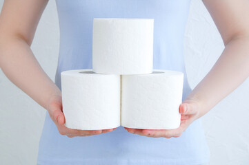 Rolls of toilet paper in the hands of Caucasian woman against the background of a white wall.