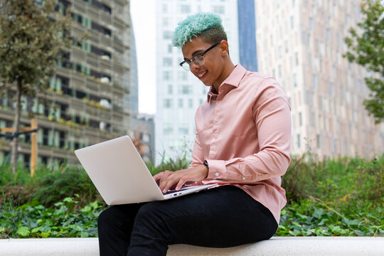 Side view low angle of happy African American male entrepreneur working on project while sitting with laptop on the street