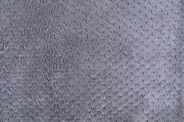 Texture of fragment of fur bedspread on gray bed.