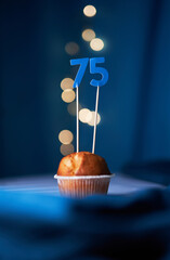 Birthday cake or muffin with seventy five (75) number and blurred lights on the blue background....