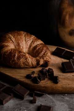 From above of delicious fresh crusty croissant and pieces of dark chocolate composed on wooden board on shabby table with linen fabric