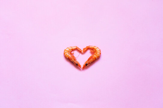 Raw prawns placed in shape of heart on bright pink background in studio
