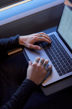 Crop young male freelancer sitting on passenger seat in modern train and typing on netbook while working during trip