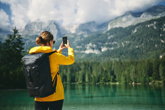 Back view of unrecognizable woman photographing high mountains on cellphone during trip in Dolomites