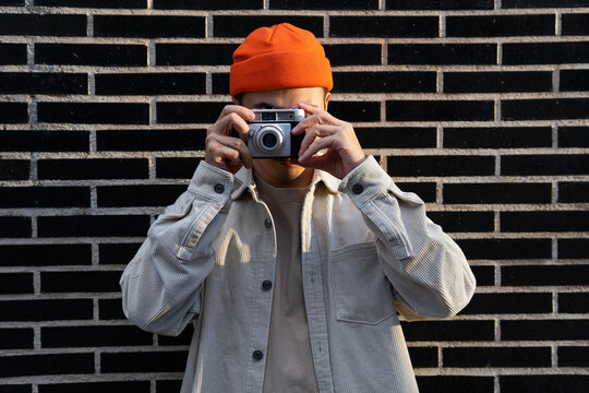 Crop unrecognizable male taking photos on camera while standing against brick wall on the street