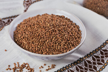 Bowl of dry raw buckwheat groats on a white wooden background. Cooking buckwheat porridge concept.