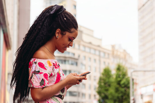 Side view ethnic female in trendy outfit text messaging on cellphone on pavement in town