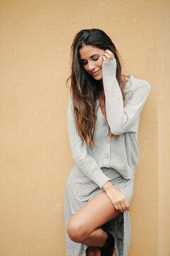 Charming female with long hair and in casual dress standing near building on street and modestly looking down