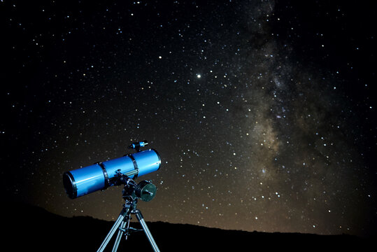 Modern optical telescope against cloudless dark sky with glowing stars at night time
