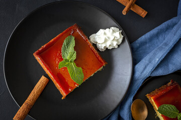Top view of black plate with portion of palatable gourmet apple pudding garnished with mint leaf and cinnamon sticks served with whipped cream with blue napkin cloth on dark background