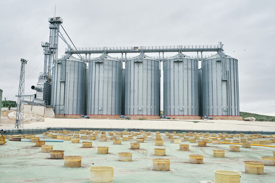 Low angle of huge steel agricultural silo towers located at factory area under cloudy sky