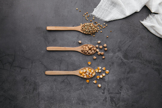 Top view of assorted dried ingredients placed in wooden spoons and scattered on black table in kitchen