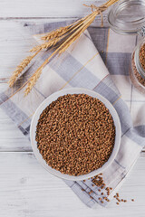 Bowl of dry raw buckwheat groats on a white wooden background. Cooking buckwheat porridge concept.