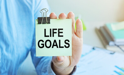 LIFE GOALS written on a voucher shown by a female businessman. Soft focus.
