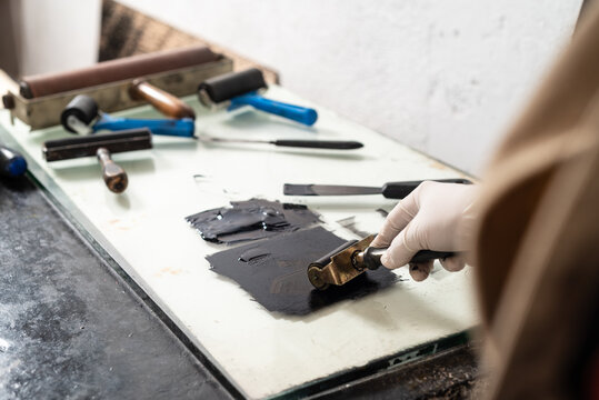 Closeup hand of crop anonymous artisan in glove using braver and spreading ink on sheet for engraving while working in professional workshop