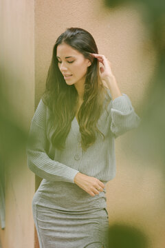 Charming female with long hair and in casual dress standing near building on street and modestly looking away