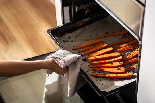 Cropped unrecognizable person getting tray with honey glazed carrots out of oven