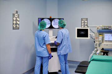 Back view of anonymous female medics in uniforms showing with fingers at display of diagnostic device in clinic