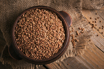 Organic uncooked scattered buckwheat grain in a bowl on a rustic wooden background. Healthy and diet food concept.