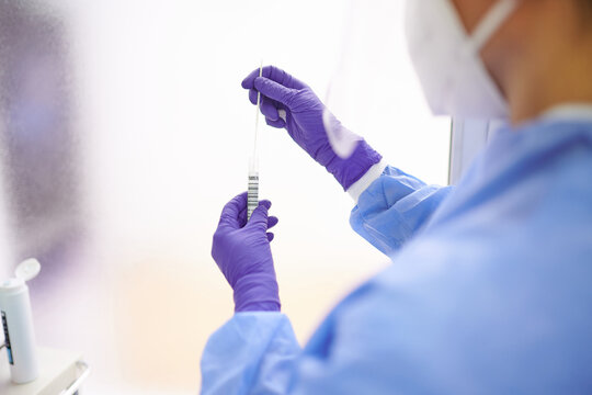 Side view of anonymous medic in protective shield taking analysis from nose of female patient while using medical tool during COVID 19 pandemic