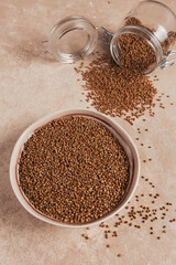 Bowl of dry raw buckwheat groats and glass jar on a light beige background. Cooking buckwheat porridge concept.