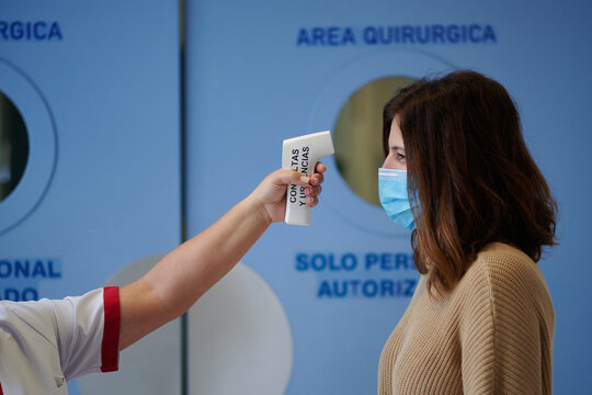 Crop unrecognizable medic in uniform measuring temperature of female patient in mask while using modern thermometer in clinic