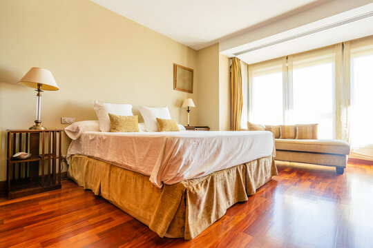 Cozy spacious bed with cushions and coverlets in room with wooden parquet and panoramic windows