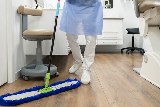 Crop anonymous medical staff in uniform washing floor with mop in modern dental cabinet