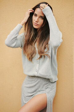 Charming female with long hair and in casual dress standing near building on street and modestly looking away