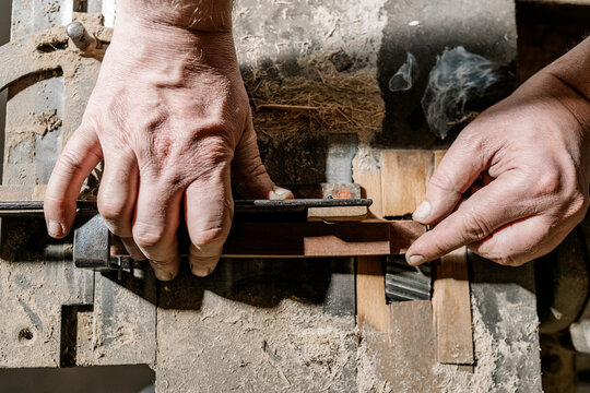 Crop male woodworker standing at old workbench and working with lumber details in grungy workshop