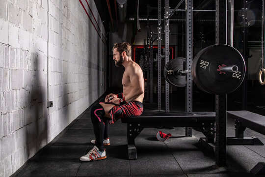 Side view of determined sportsman with strong naked body sitting on bench press with barbell and getting ready for workout
