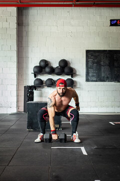 Muscular male with strong naked torso doing exercises with dumbbell in gym and looking at camera