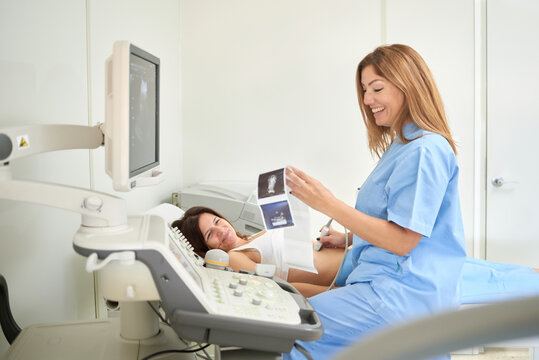 Female medic checking ultrasound pictures near professional equipment and anonymous patient during sonography diagnostic in clinic