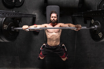 From above of strong focused male athlete lying on bench press and doing exercises with heavy barbell during workout in gym